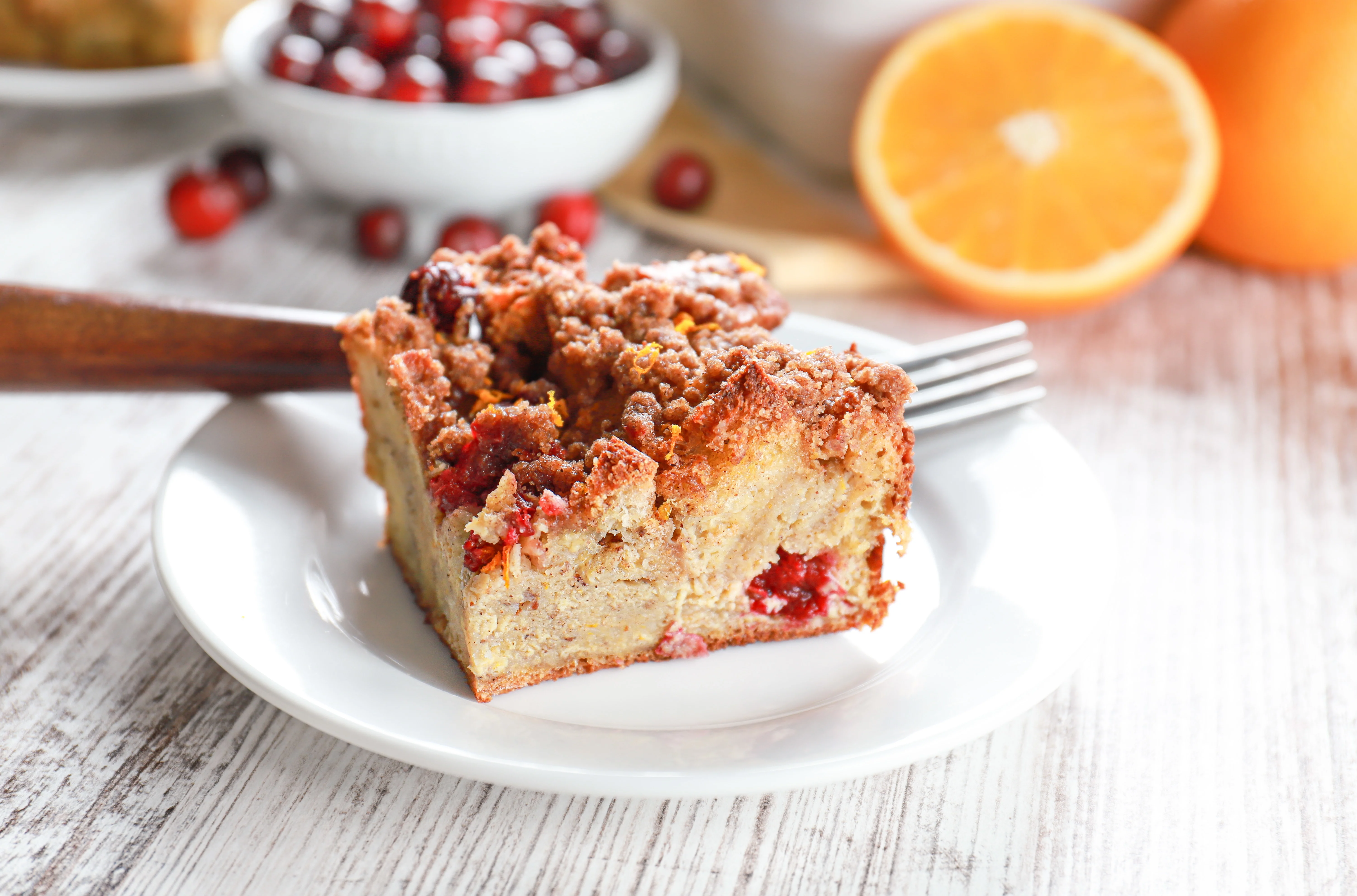 Slice of cranberry orange french toast casserole on a small white plate with remaining french toast casserole in the background.