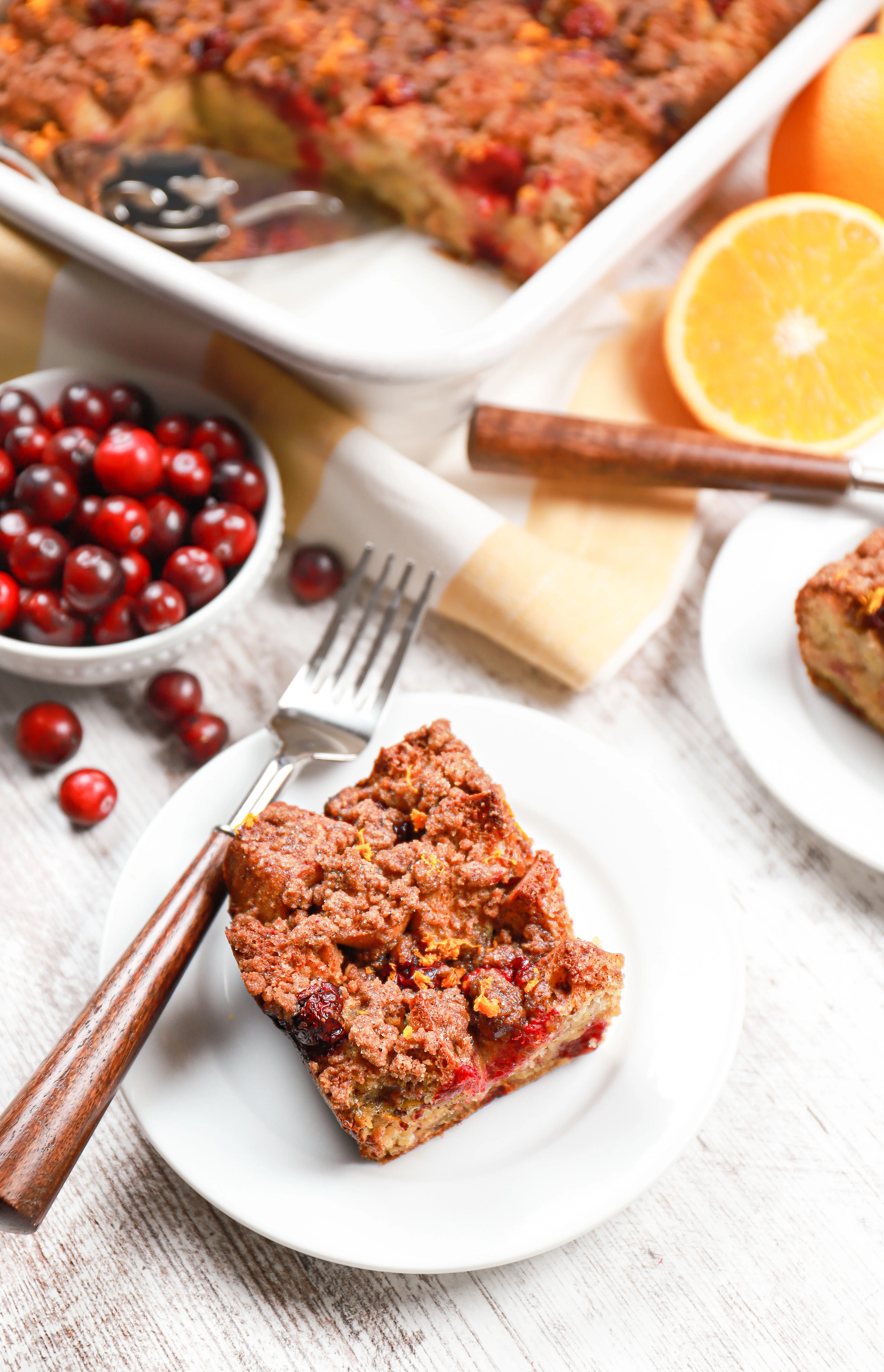 Overhead view of a piece of cranberry orange french toast casserole on a small white plate with remaining french toast casserole behind it.